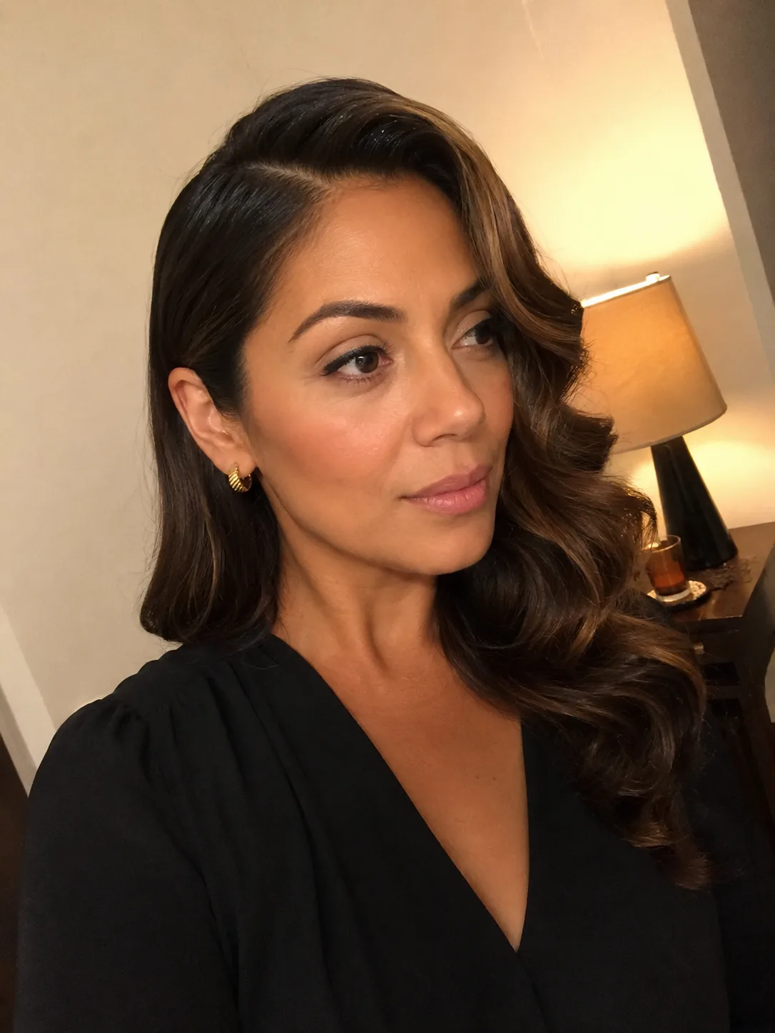 A close-up indoor selfie of a smiling woman showcasing a short, voluminous asymmetric wavy bob with warm copper highlights.