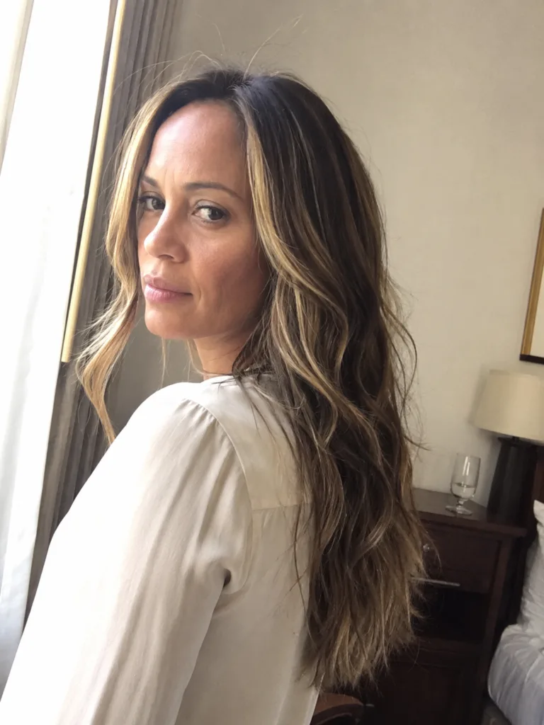 A close-up portrait of a woman showcasing long, layered light brown hair styled with bright blonde face-framing money piece highlights.