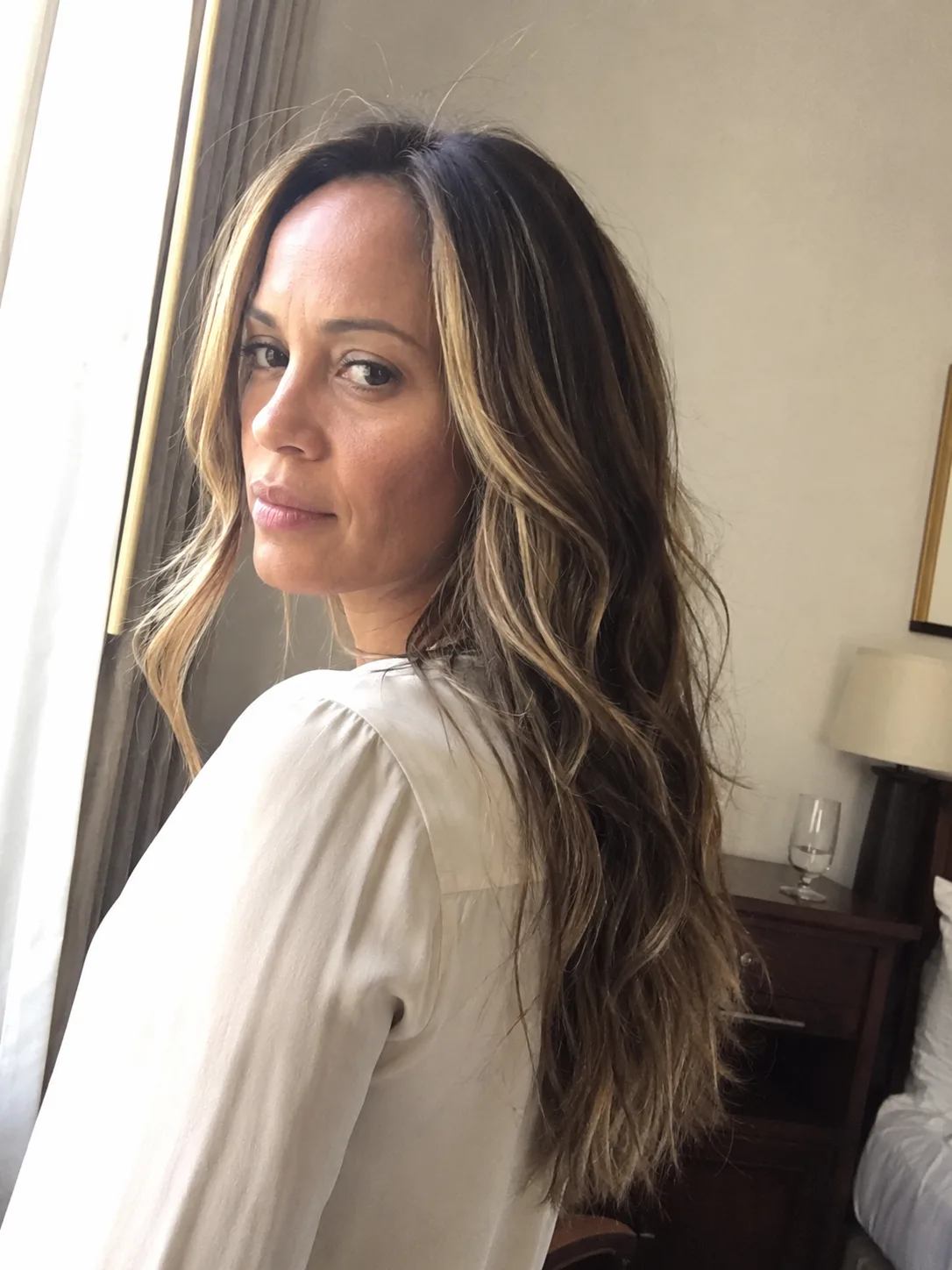 A close-up portrait of a woman showcasing long, layered light brown hair styled with bright blonde face-framing money piece highlights.