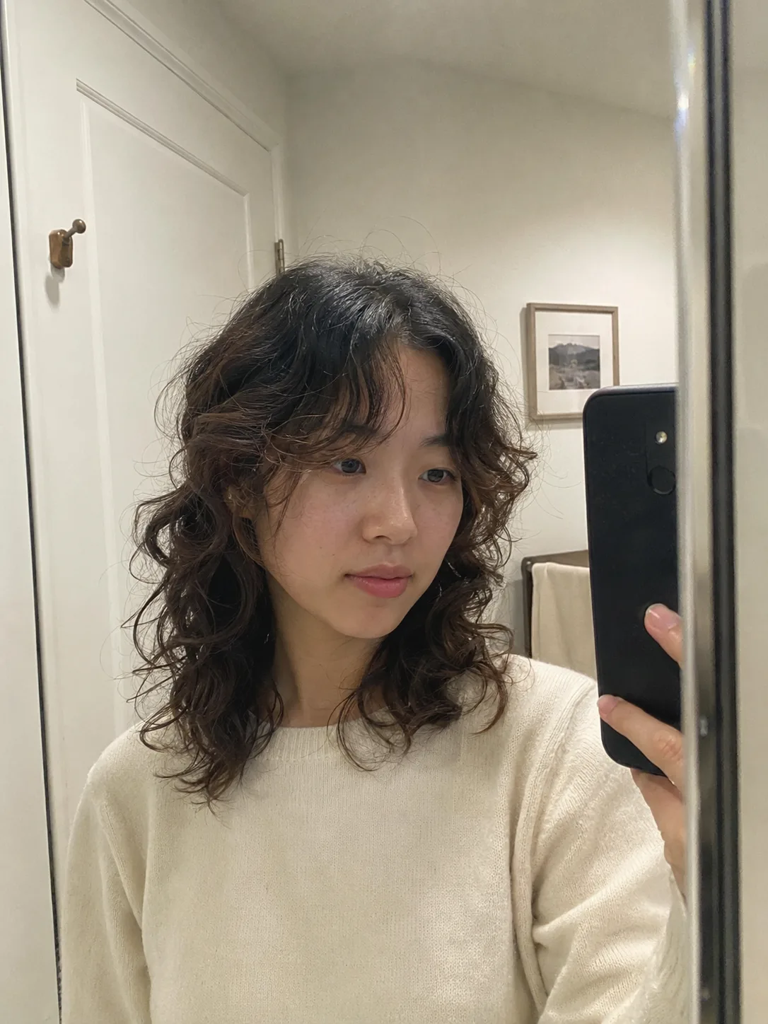 A close-up portrait of a woman showing a sleek, wet-look curly hairstyle with defined side parts and precisely styled baby hairs along the hairline