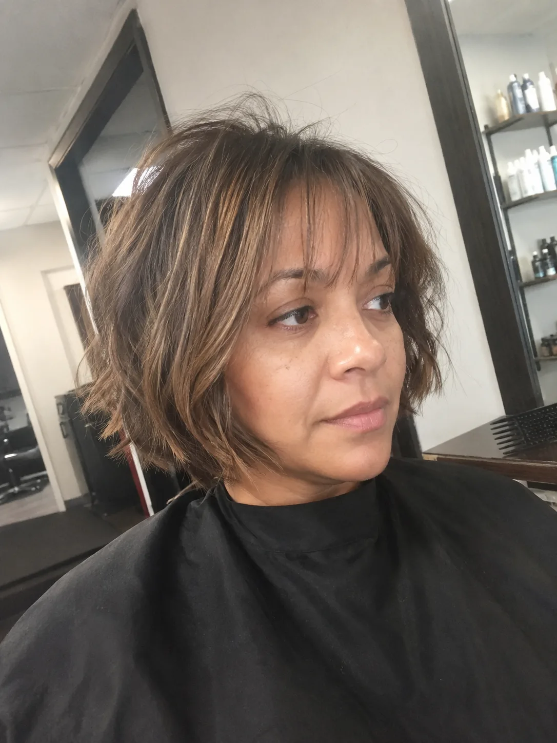 A close-up portrait of a woman with a messy, textured brown pixie cut featuring soft, layered bangs framing her forehead naturally.