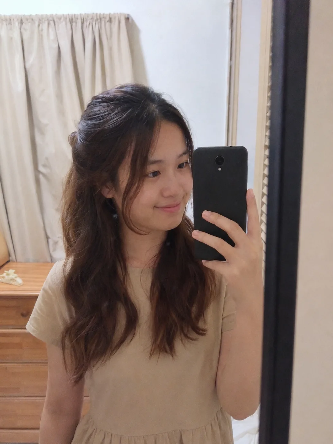 A cozy indoor selfie of a woman looking toward the camera with a gentle smile, displaying a messy, textured shoulder-length haircut with voluminous dark brown waves and soft h
