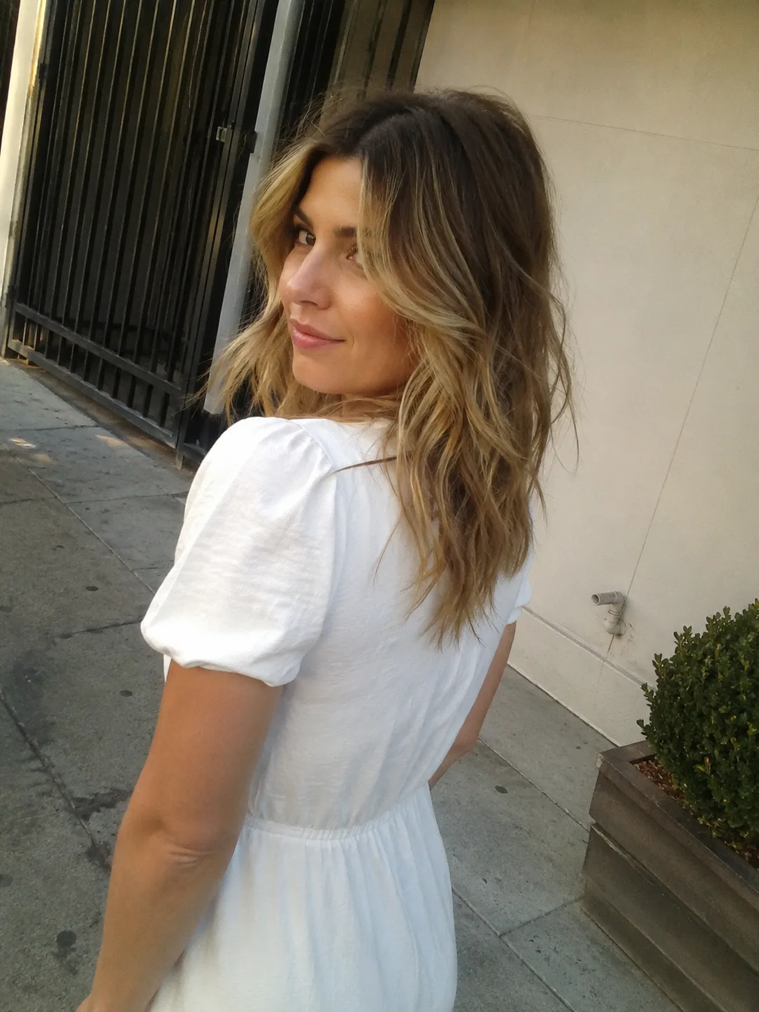 A direct portrait view showcasing a woman with naturally dark, defined springy curls styled into a medium-length layered haircut that rests at the collarbone.