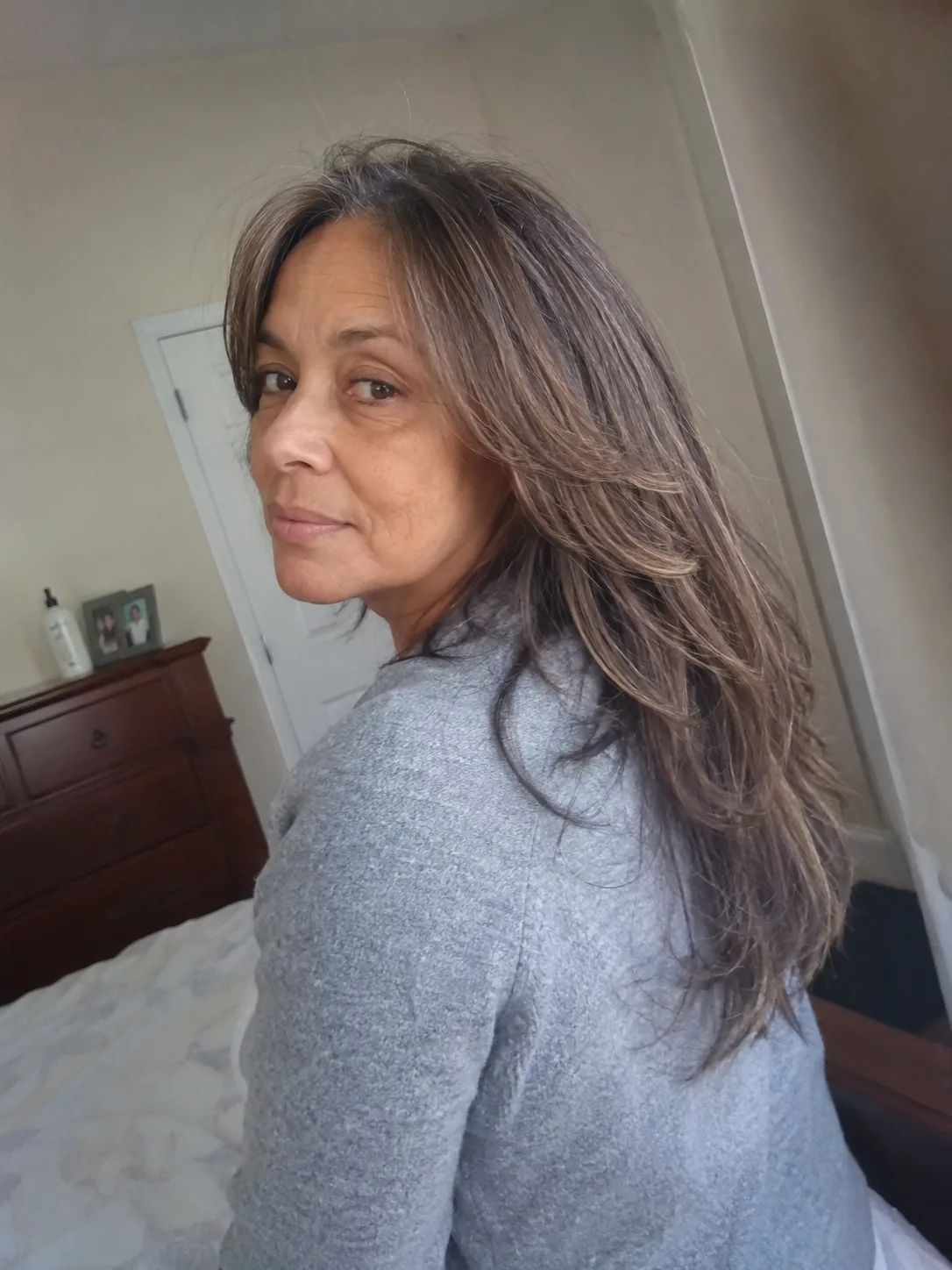 A front view of a mature woman smiling, showcasing long, fine grey hair parted down the middle that flows naturally past her shoulders