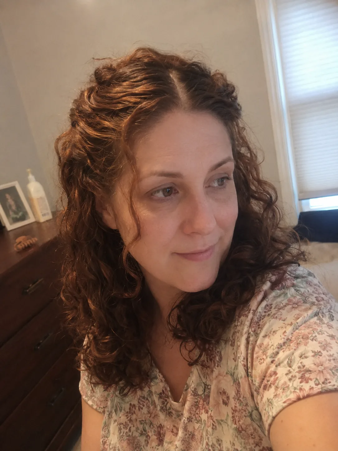 A mirror selfie of a woman displaying a shoulder-length curly hairstyle with a thick set of textured, curly curtain bangs framing her face