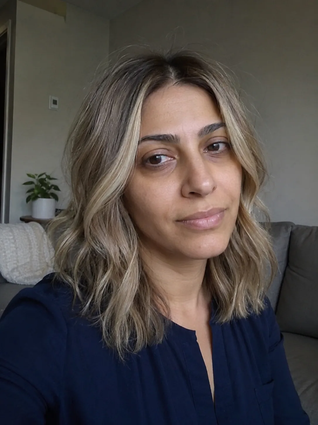 A mirror selfie of a woman displaying a straight, shoulder-length lob with dark roots transitioning into a pale blonde ombré finish