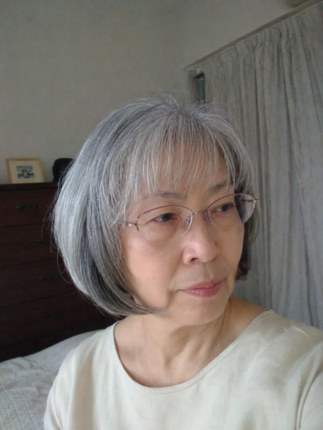 A mirror selfie of a woman wearing glasses, showcasing a classic, sleek chin-length straight grey bob haircut