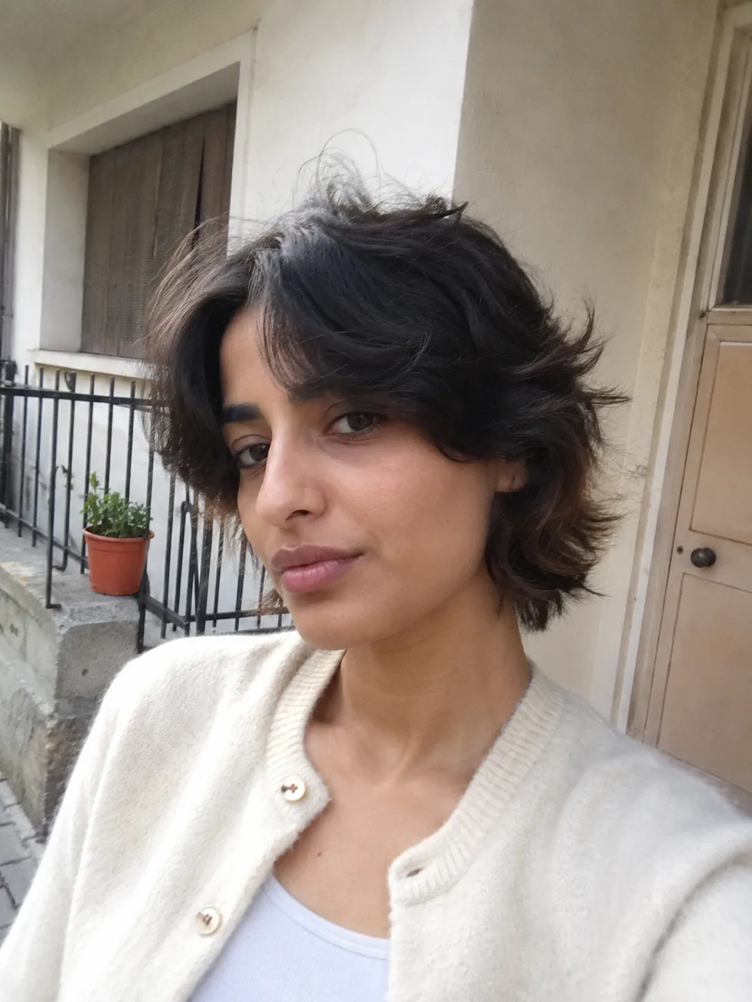 A mirror selfie of a woman with a relaxed, dark shaggy haircut featuring wispy curtain bangs split gently down the middle