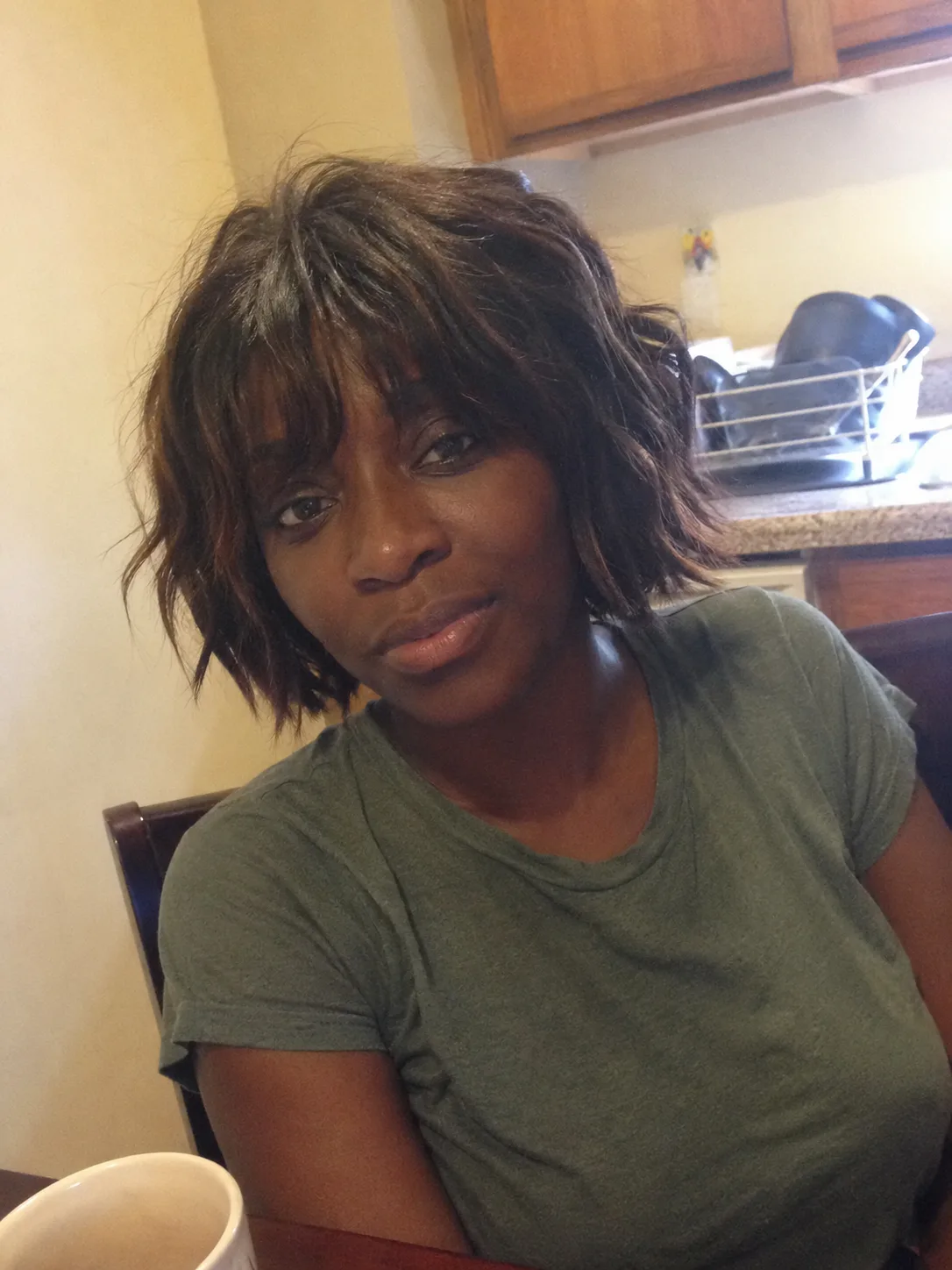 A mirror selfie of a woman with a sleek, straight jet-black bob haircut featuring a thick, blunt fringe cut straight across the forehead