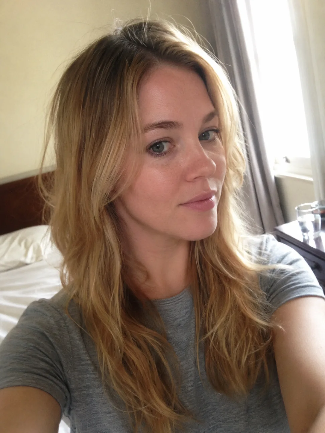 A mirror selfie of a woman with long, dark textured hair featuring effortless curtain bangs and lived-in layers framing her face