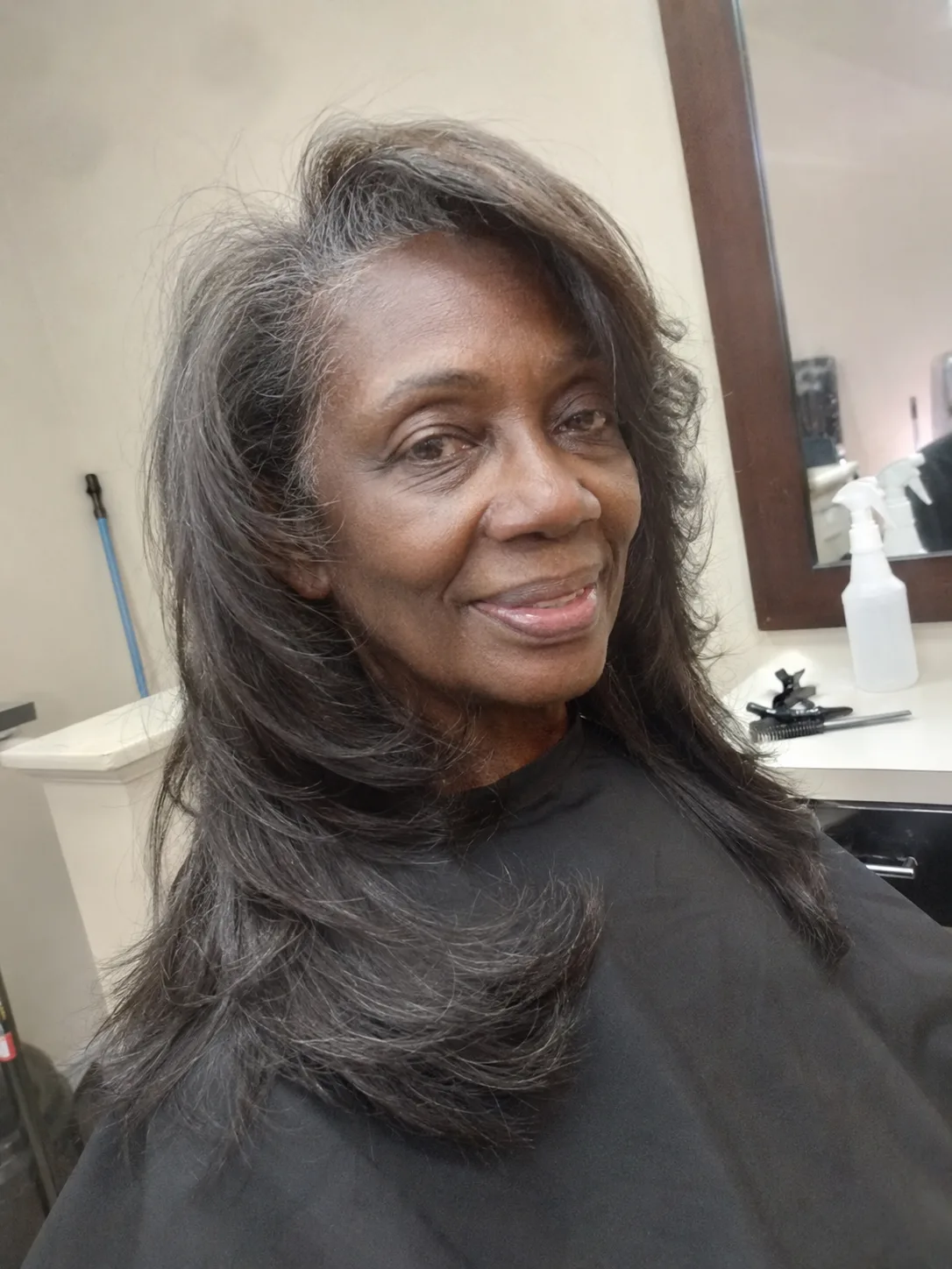 A mirror selfie of a woman with long grey hair, showing a slightly thinner midshaft area while maintaining density at the root