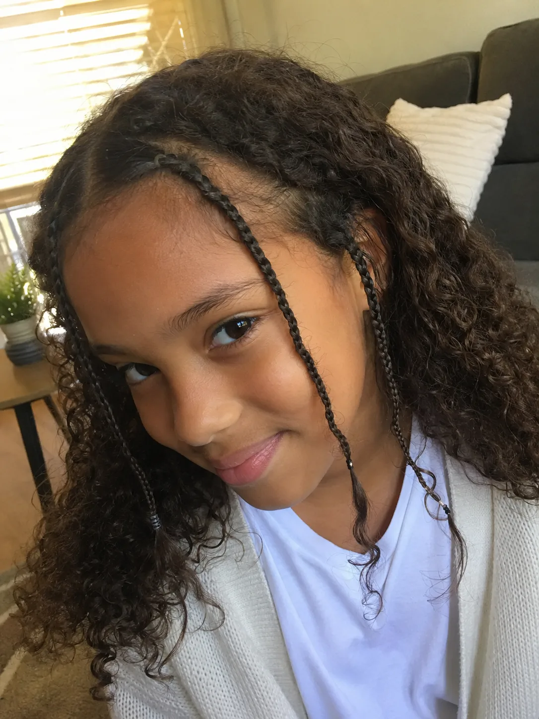 A mirror selfie portrait of a smiling young girl with shoulder-length curly light brown hair kept neat with a simple pink headband