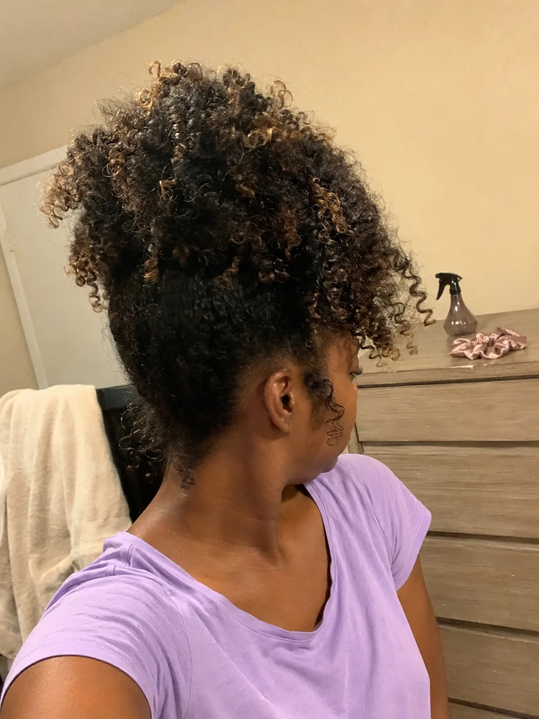 A person with shoulder-length, curly hair and bangs, checking their appearance in a mirror