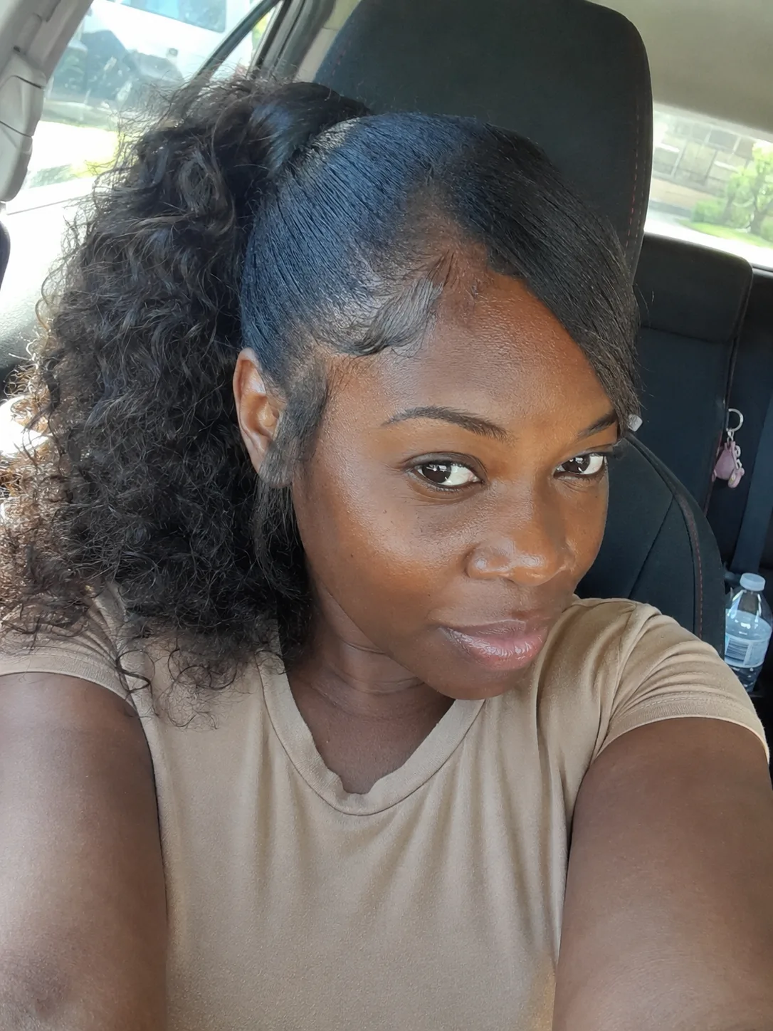 A polished high ponytail featuring a smooth, side-swept front section and deeply defined natural curls