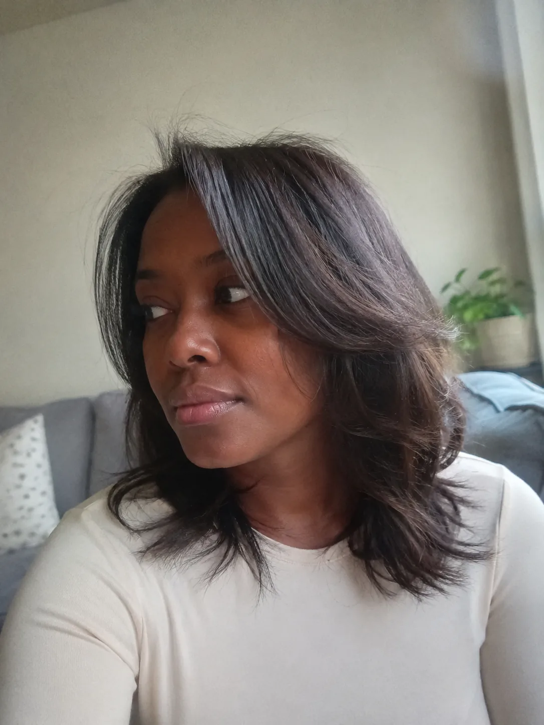 A portrait of a woman displaying a soft, wavy curly layered haircut with a defined structural weight line at the perimeter