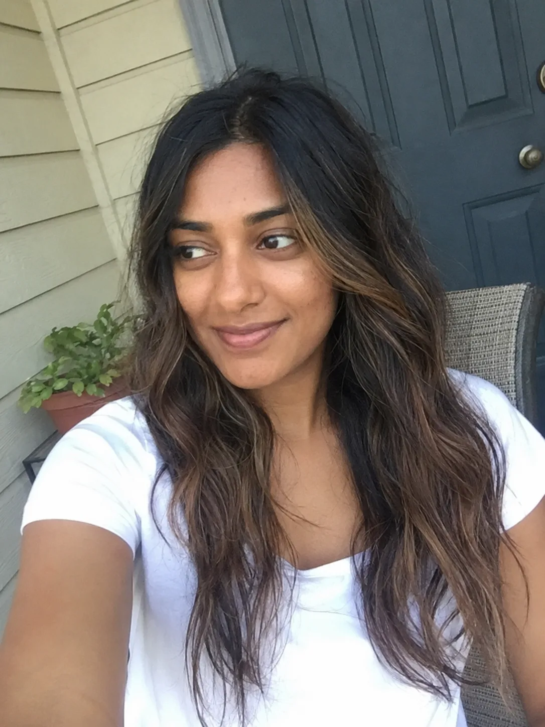 A portrait of a woman looking aside in soft sunlight, showcasing her long, texturized light brown hair with dimensional blonde highlights and soft face-framing layers