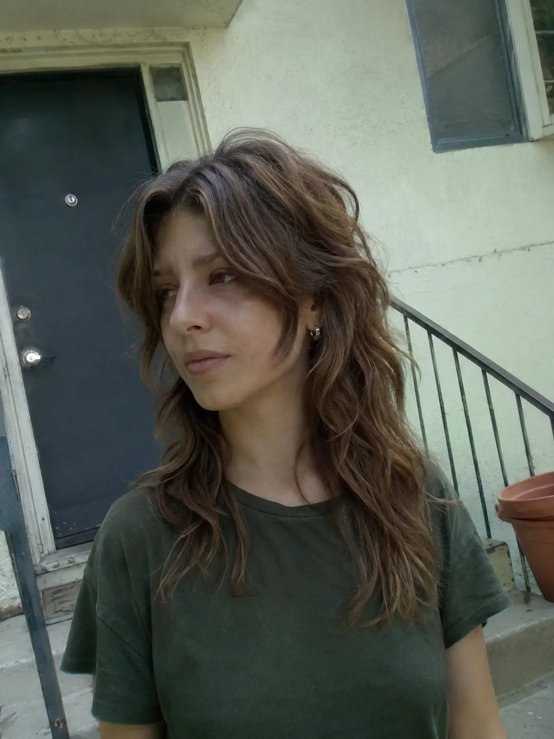 A portrait of a woman looking slightly away, showcasing her long, thick dark brunette hair with layered, bouncy face-framing waves and subtle highlights