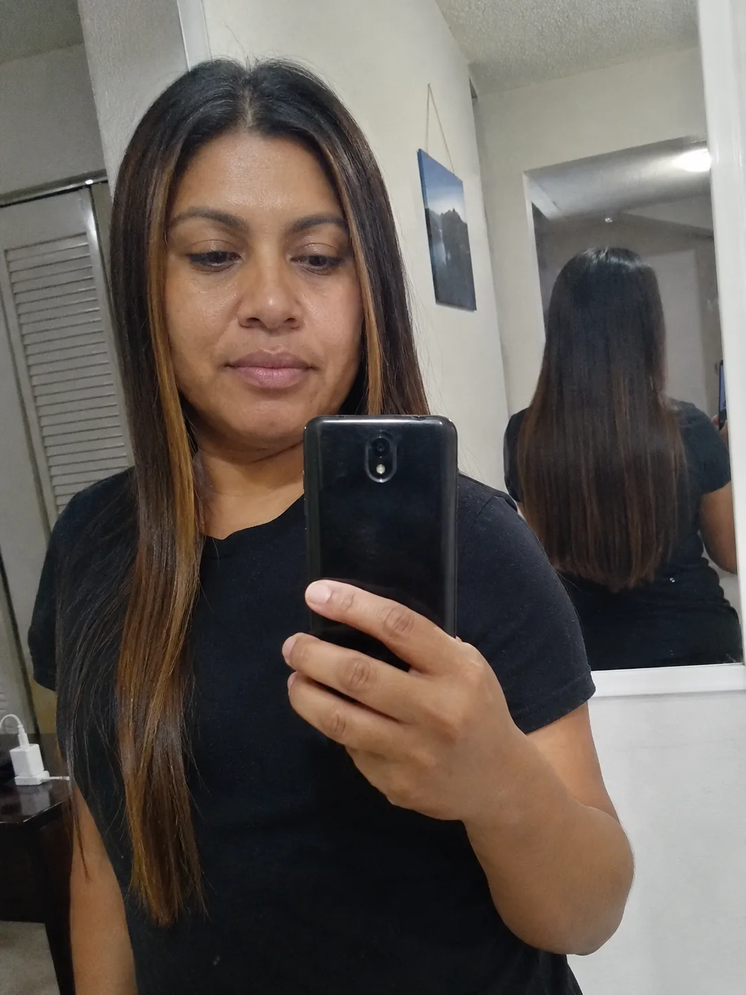A portrait of a woman looking to the side, displaying her long, voluminous dark hair styled with soft, cascading layers and subtle auburn highlights