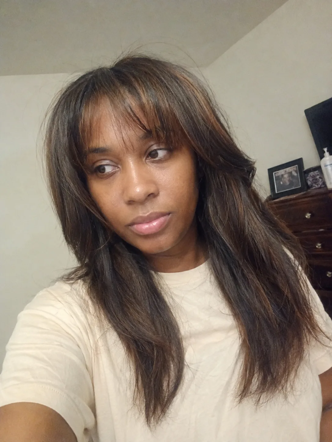 A portrait of a woman with long, voluminous dark brown hair styled with soft, cascading curls at the ends and subtle layers