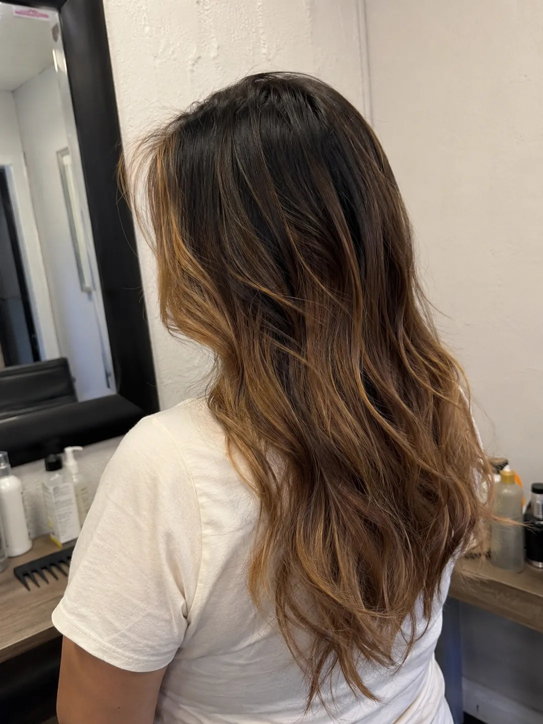 A portrait of a woman with voluminous, bouncy curly hair featuring a dark base color beautifully accented with honey blonde and golden highlights throughout the curls