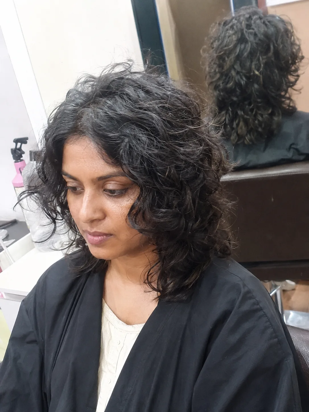 A profile portrait of a woman looking toward a window, showcasing a dense, voluminous head of natural, tightly coiled black hair shaped into a rounded curly afro