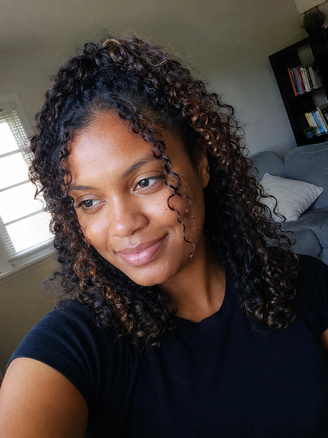 A selfie of a woman with a half up top knot and loose strands framing the face