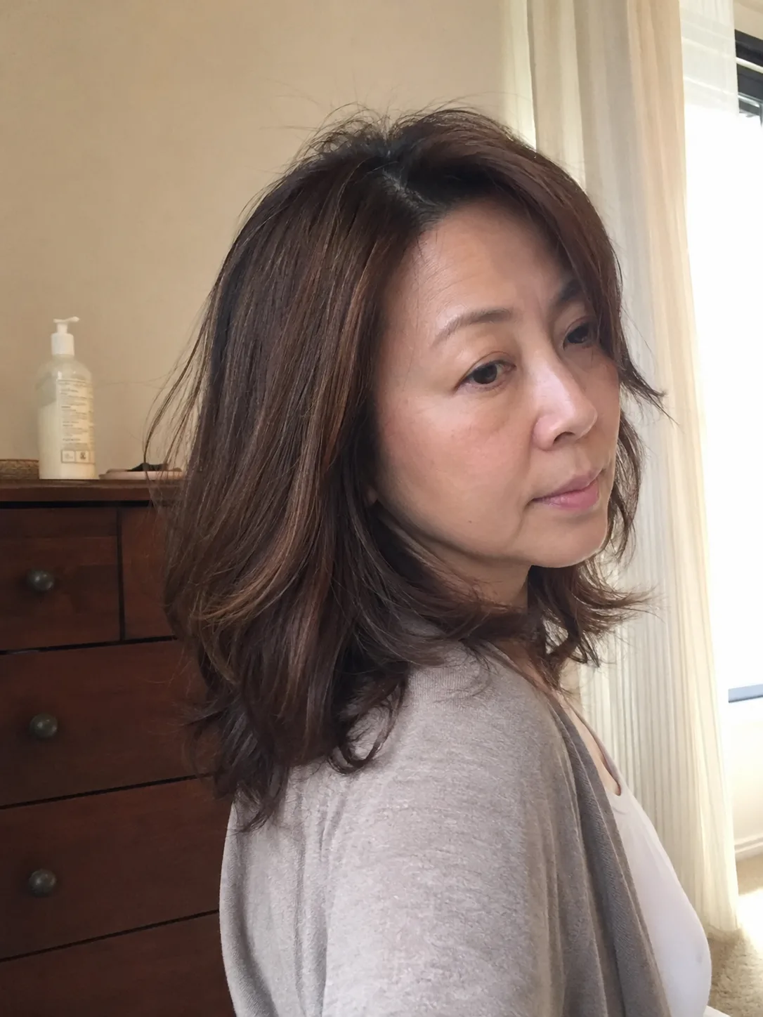 A side-angle view of a woman showcasing the back and side flow of a medium length layered haircut, showing how the weight sits below the occipital bone