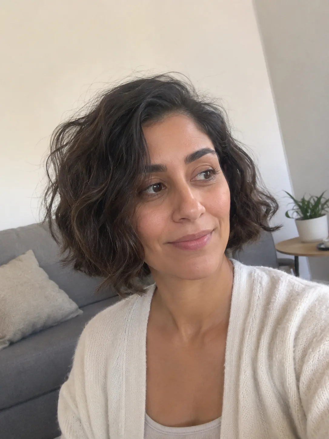 A side-profile mirror selfie showing a woman's dark, thick hair gathered up securely into a messy, frizzy bun held together by a tortoiseshell claw clip