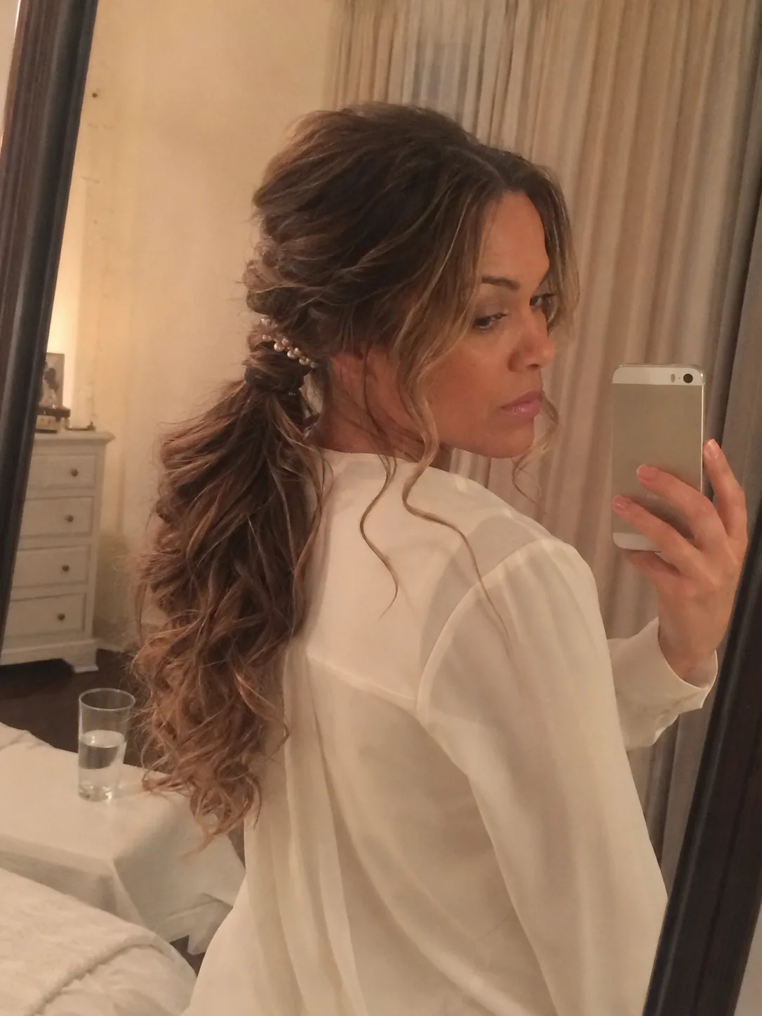 A side profile of a woman with a loose, low, wavy ponytail that is twistedsecured at the sides