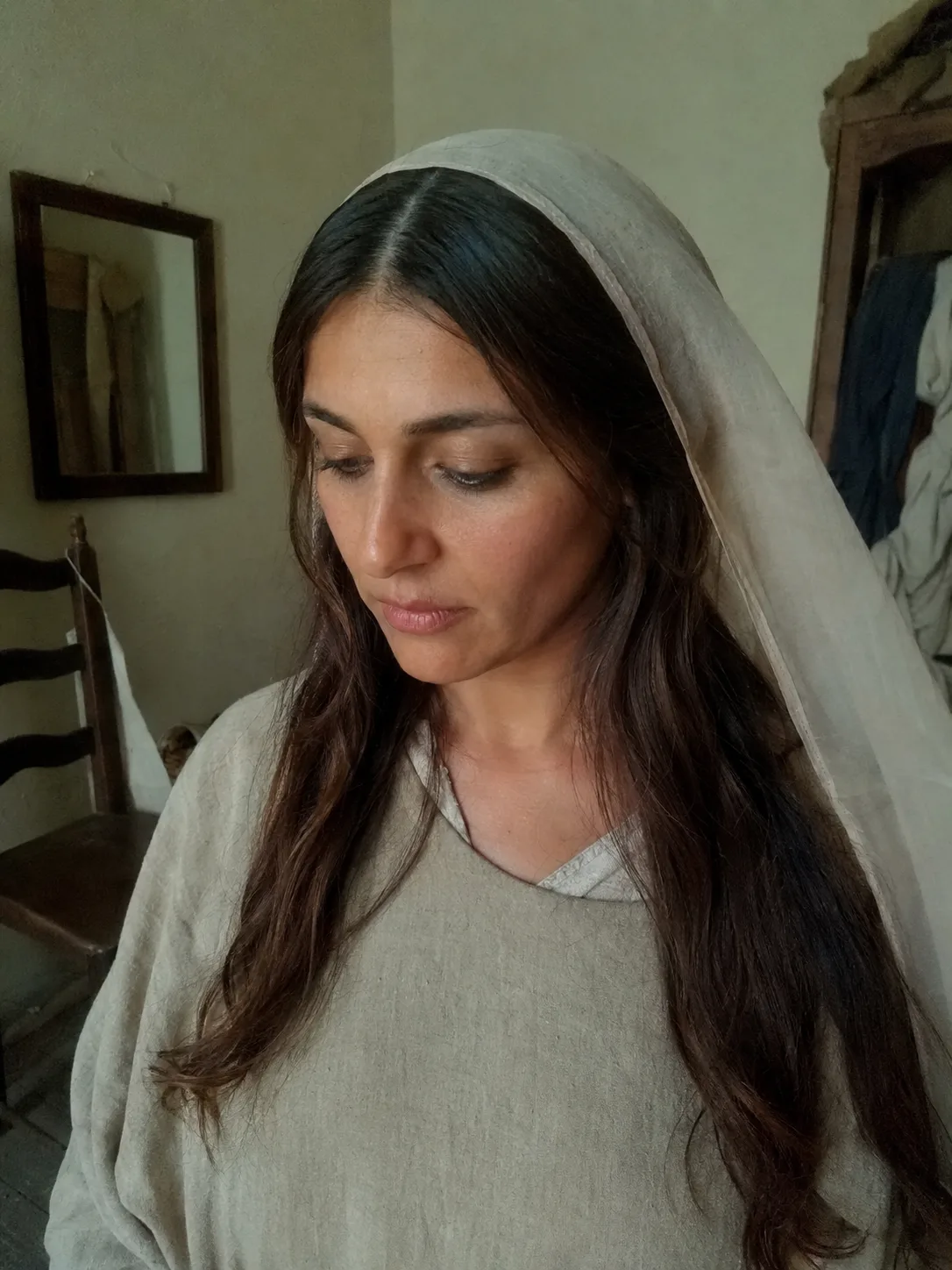 A side profile view of a woman outdoors looking into the distance, wearing a white flowing peasant dress