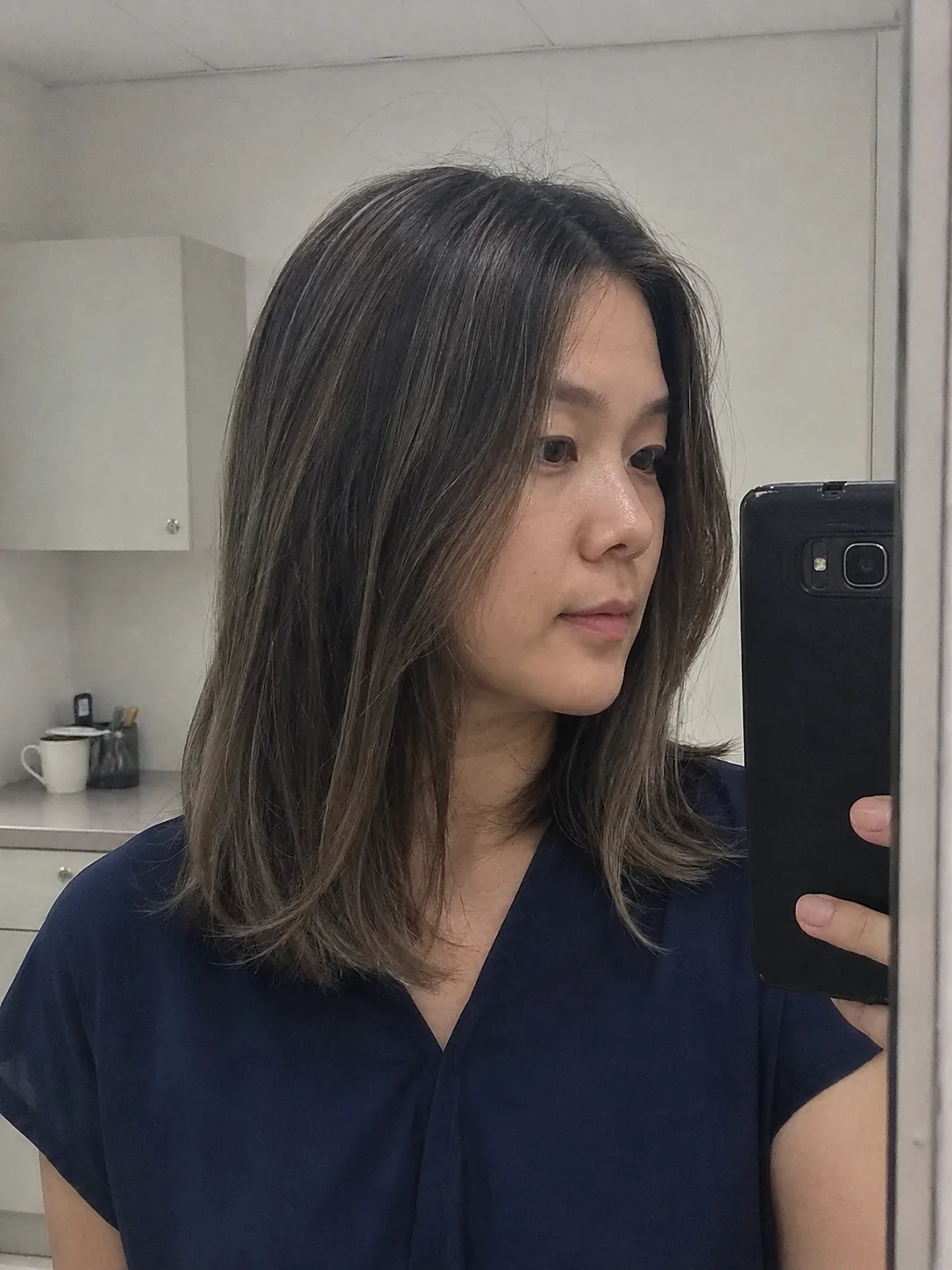 A side profile view of a woman showcasing a sharp, chic, straight platinum blonde bob haircut with subtle shadow roots