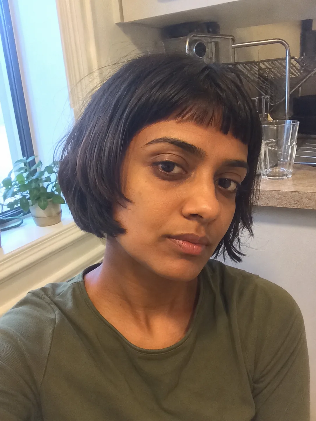 A side profile view of a woman showcasing a sleek, dark asymmetrical bob with sharp lines and a clean side-swept fringe