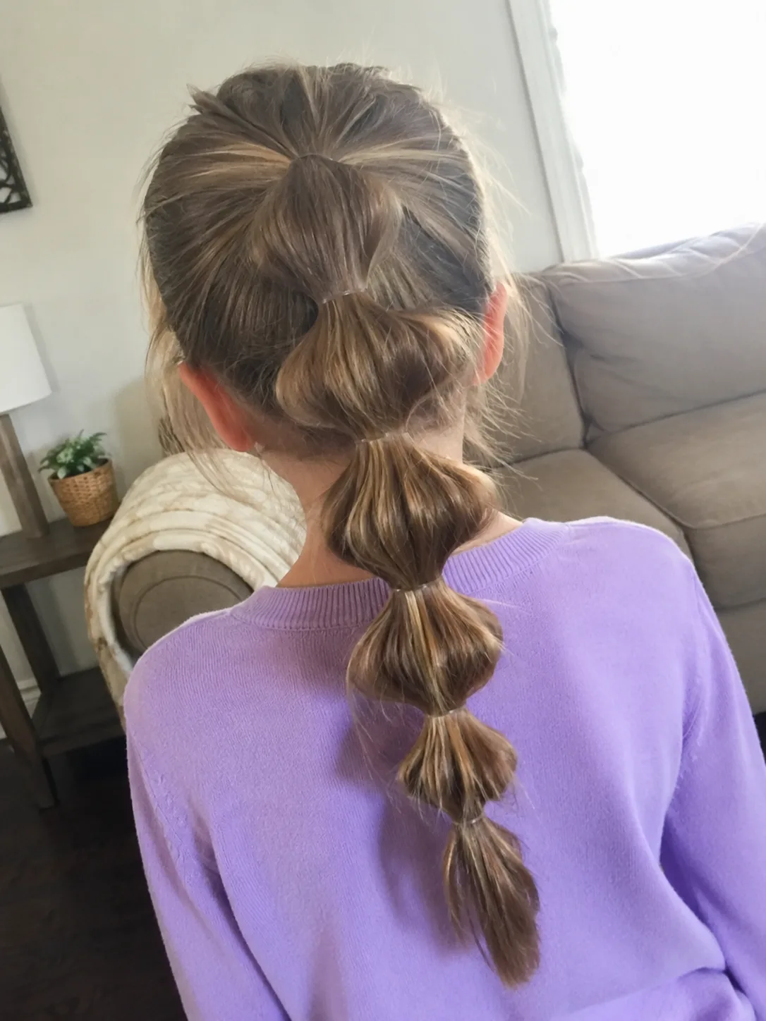A side profile view of a young girl showing her sleek, slicked-back natural hair neatly gathered into a large, intricate, and tightly braided high bun