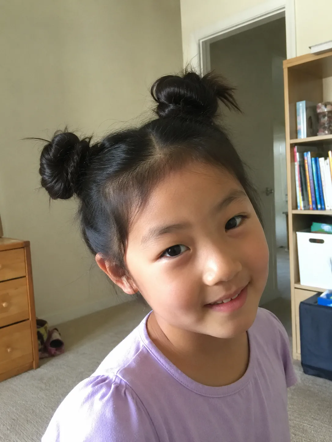 A side profile view of a young girl with naturally wavy brown hair gathered into a low, relaxed messy bun at the nape of her neck