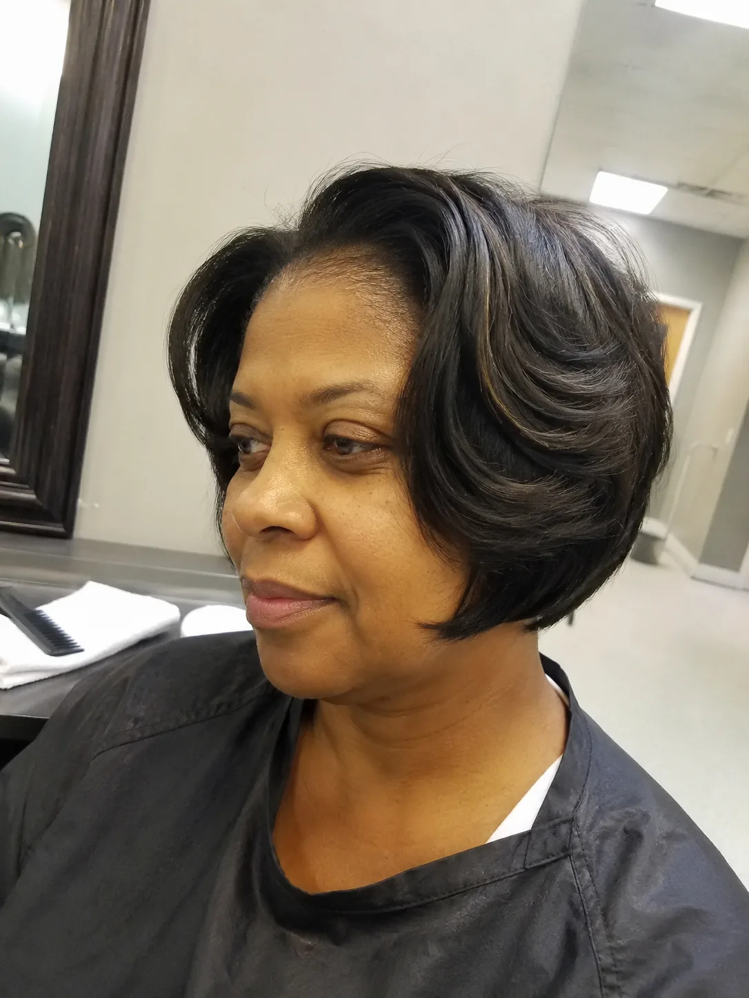 A smiling woman with a textured silver pixie haircut featuring an asymmetrical, long side-swept fringe and voluminous crown layers