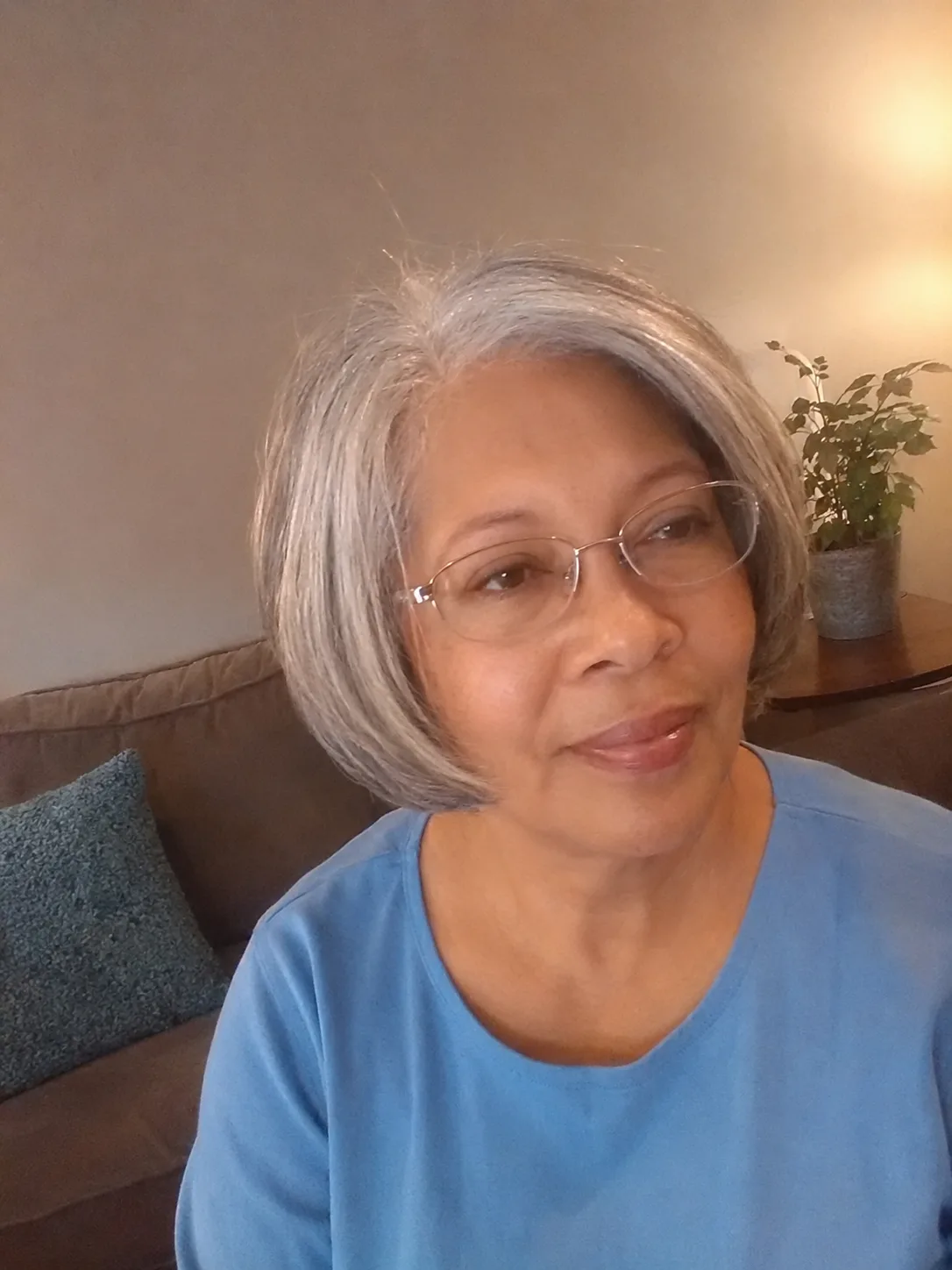 A woman in a salon cape wearing glasses, showing off a short, textured grey pixie cut with sideswept bangs