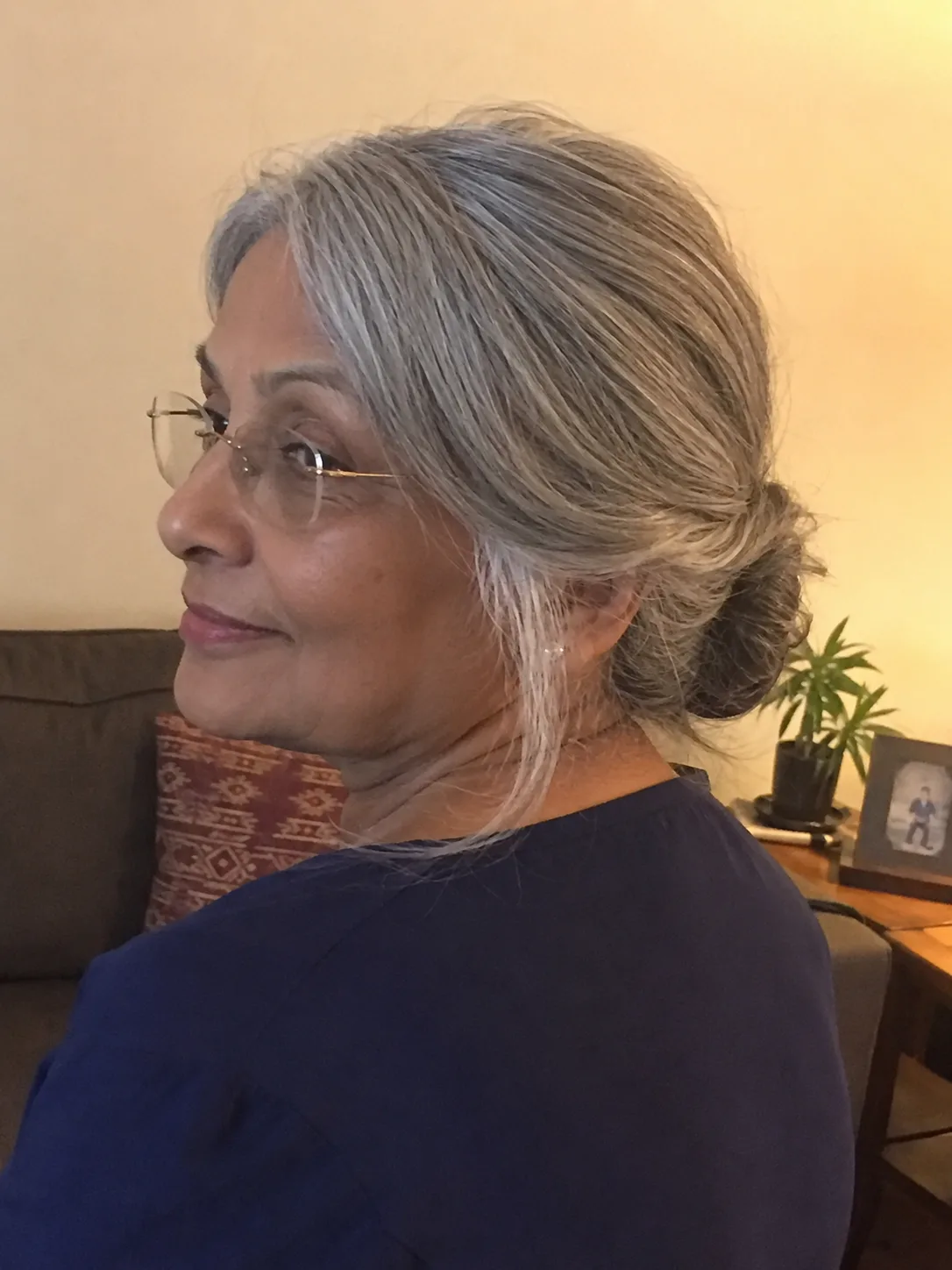 A woman looking to the side while wearing glasses, showcasing a thick, highly defined curly grey bob haircut