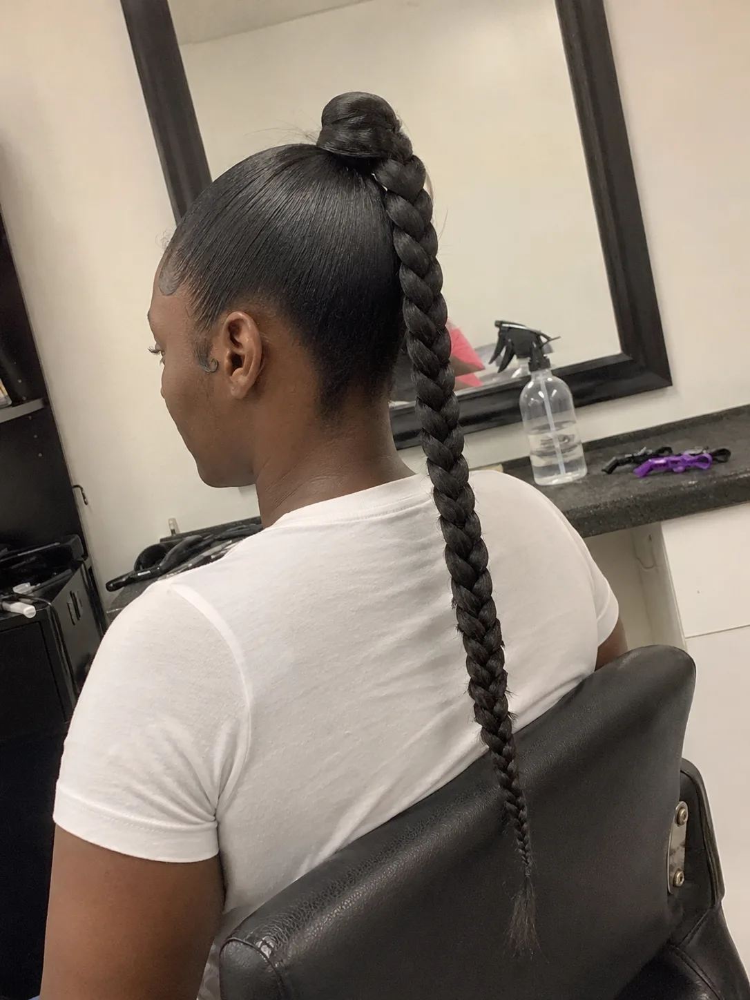 A woman seen from behind, wearing a sleek, low, straight ponytail wrapped with a section of hair at the base