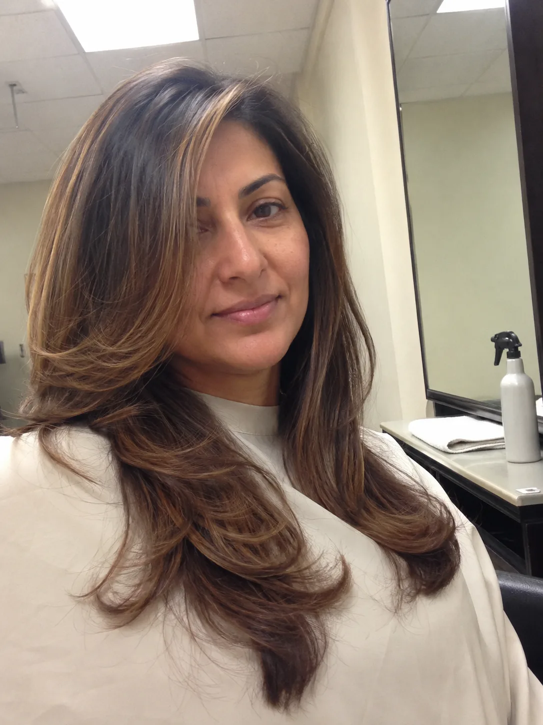 A woman taking a mirror selfie showing long dark hair with bright blonde money piece highlights framing her face