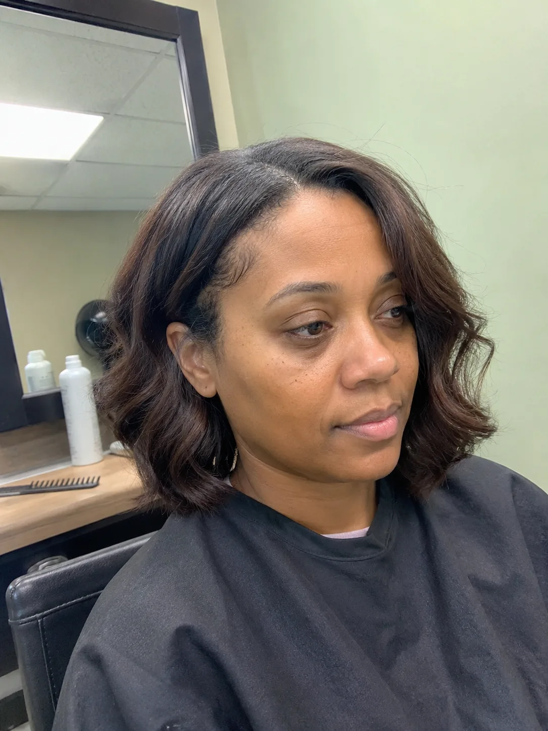 An indoor profile-view mirror selfie of a woman using a phone to showcase her dark brown wavy hair pinned up loosely in a tortoiseshell claw clip