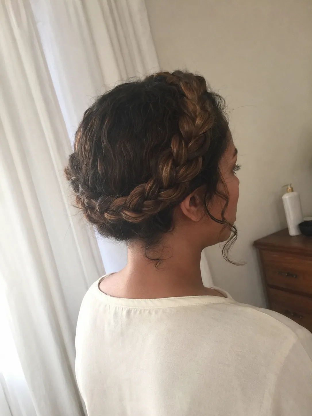 Back view of a half-up Celtic hairstyle featuring multiple small, intricate braids woven into a criss-cross pattern over loose, wavy blonde highlighted hair