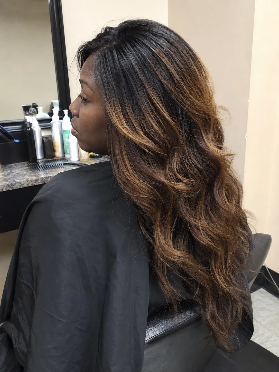 Long, cascading wavy dark brown hair with subtle ash-brown highlights, viewed from a side-angled back profile