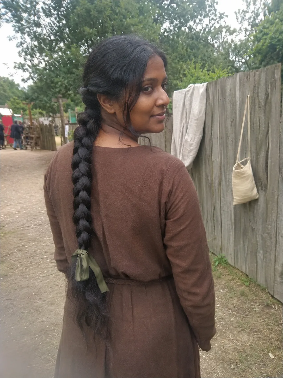 Over-the-shoulder view of a woman outdoors with wavy brown hair styled in a medieval half-up look with a prominent center part and twisted side strands