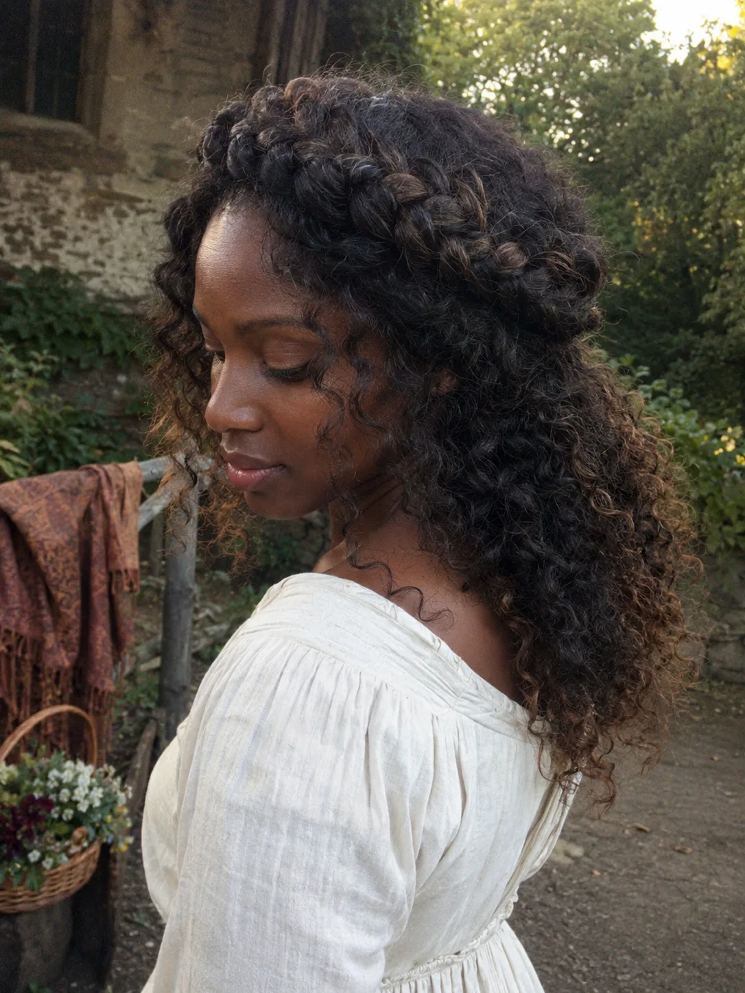 Profile view of a woman looking over her shoulder with her hair styled into a medieval coronet crown braid covered by a sheer cream veil