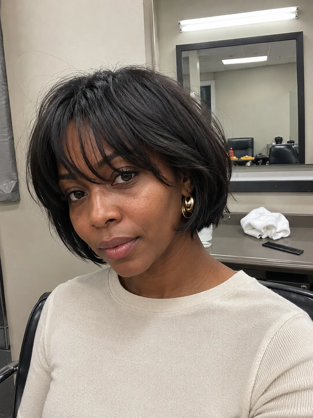 Side profile view of a woman with a precision-tapered short dark pixie cut, featuring stacked volume at the back and a neat ear-line clearance