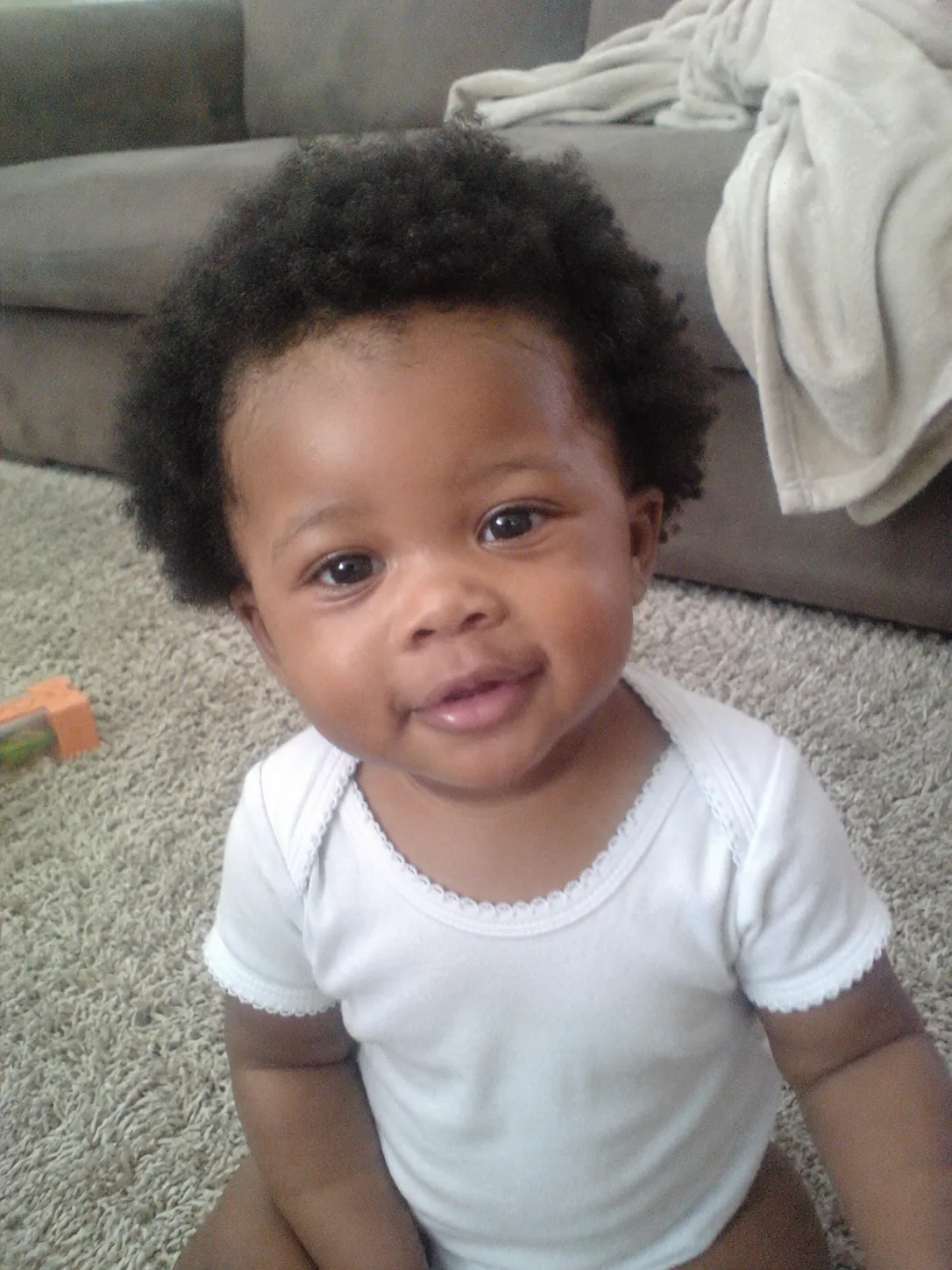 Side view of a fourteen-month-old infant showcasing fine baby hair with a single clean parting down the back