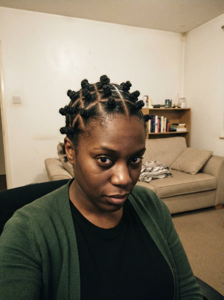 The hair is black and styled in Bantu knots, with a medium length that is past the shoulders