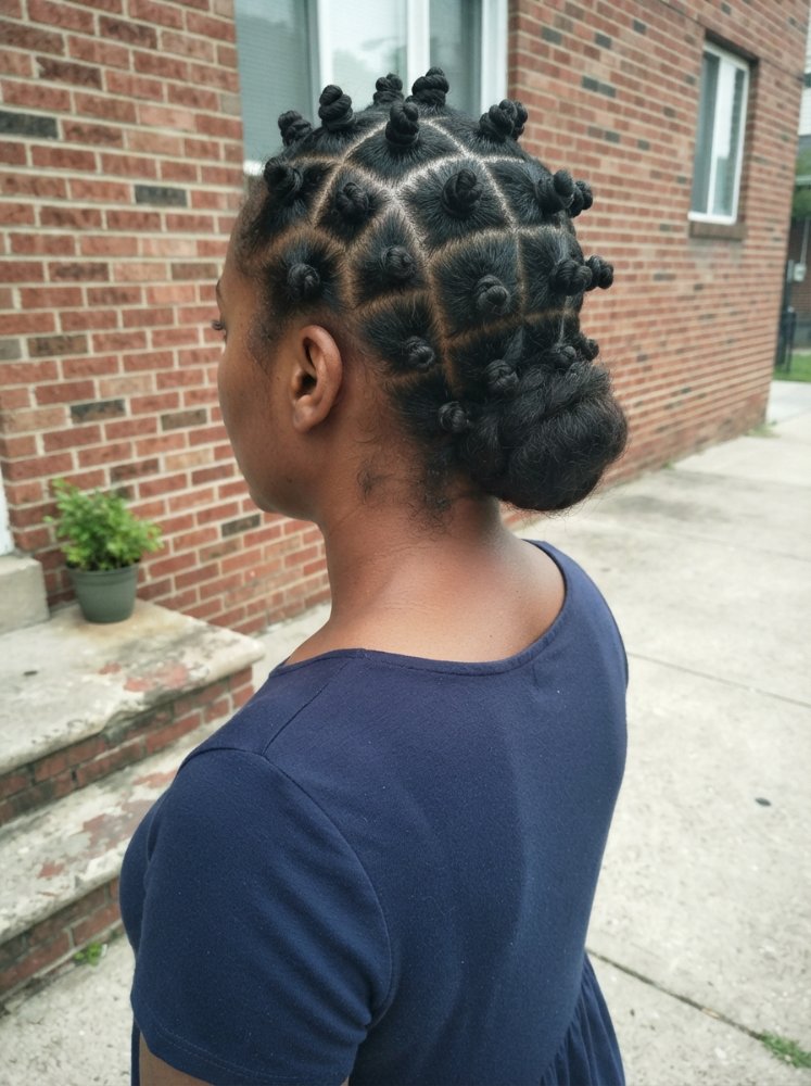 The hair is black and styled in a braided updo with small buns, secured into a low bun
