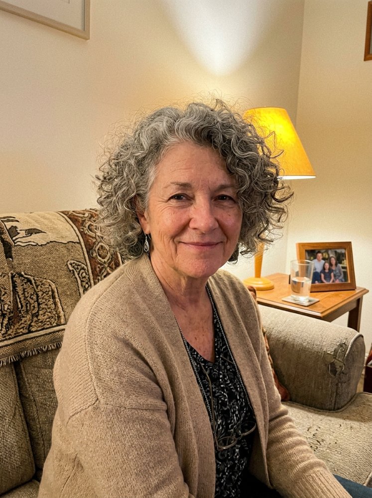 The hair is curly and shoulder-length, with a predominantly gray color that has subtle hints of brown and blonde undertones