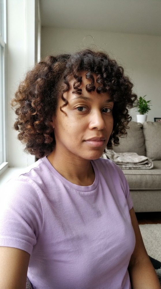 The hair is curly and shoulder-length, with a rich, dark brown color that appears to have subtle dimension and texture